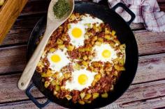 One-pot Corned Beef Hash served with eggs and dried parsley on a wooden spoon on the side of a cast iron pan