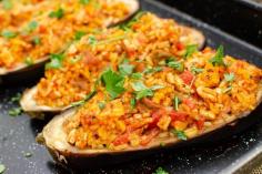 Turkey and Rice Stuffed Aubergine all cooked in a black baking tray and chopped parsley being sprinkled over the top